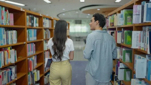 Back view of two university student walking while chatting in university library Stock Footage 326640536