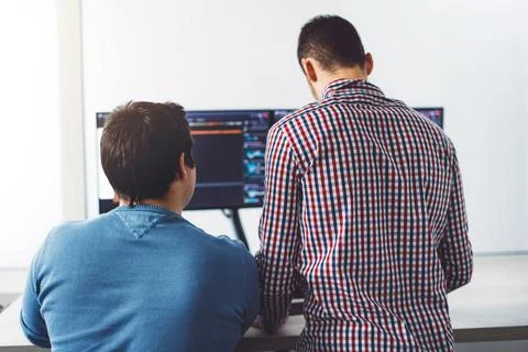 Back view of two young IT guys in front of computer screens, writing a new code 写真素材