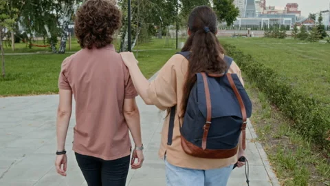 Back View of Two Young Women Walking Together along Park Road Vídeo Stock 288831482