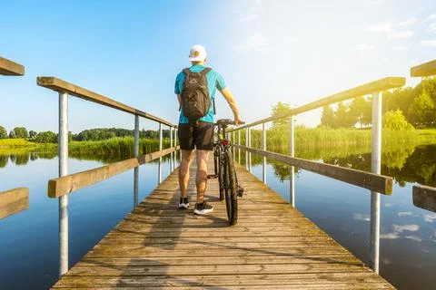Back view of unrecognizable man with bicycle on wooden bridge on sunny day Stock Photos