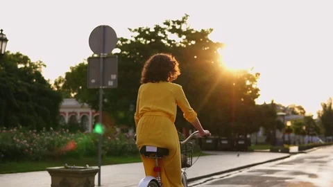 Back view of an unrecognizable woman in long yellow dress riding a city bicycle Stock Footage 79476830