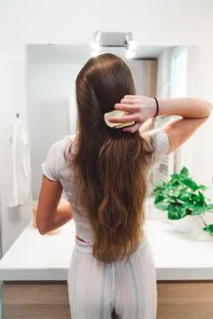 Back view, vertical photo unrecognizable woman brushing her long brown hair Stock Photos