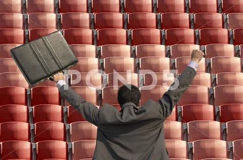 Back view of victorious businessman with briefcase facing rows of red seats at Stock Illustration