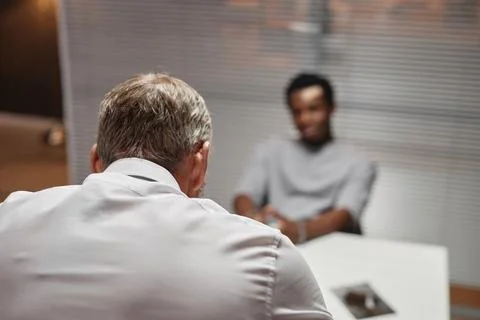 Back view of white haired detective interrogating criminal suspect Stock Photos