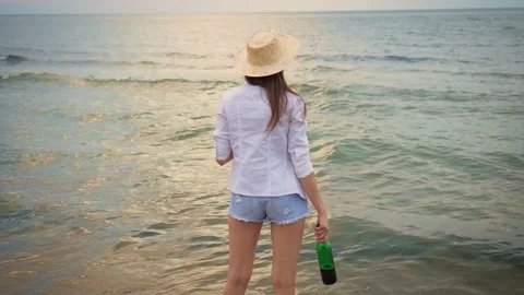 Back view Woman, adorned in straw hat and white shirt, holds wine bottle in her Video stock 254082004