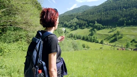 Back view of a woman with backpack blowing the pollen of a dandelion flower. In  Stock Footage 302899510