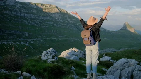 Back view of woman in hat with backpack raises her hands Stock Footage 136592071