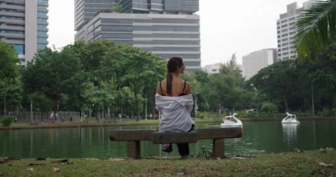 Back view of woman sitting on bench in Bangkok park water lake and skyscrapers Stock Footage 271008595