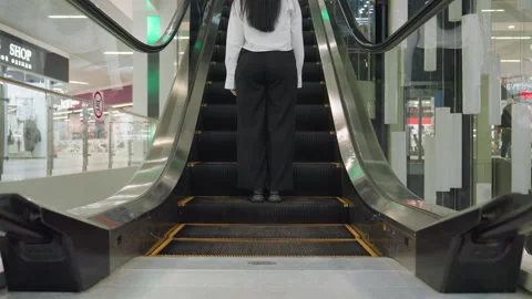 Back view of woman stepping onto moving escalator inside modern shopping mall Stock Footage 310142580