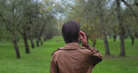 Back view of woman walking in spring garden among green trees rainy weather Stock Footage 154339622