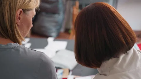 Back view of women discussing materials with colorful fabric samples on table Stock Footage 307135913