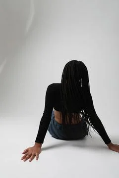 Back view of Young African American woman sits on the studio floor. Vertical. 스톡 사진