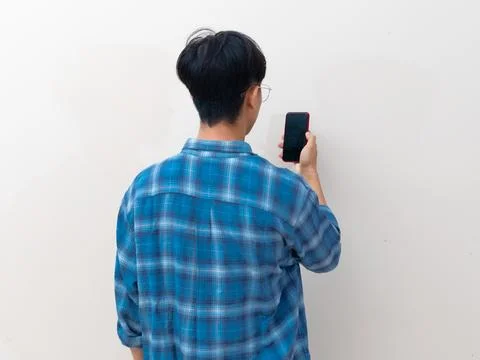 Back view of a young Asian man holding a smartphone against a plain backgroun Stock Photos