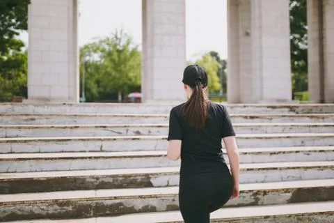 Back view of young athletic strong brunette girl in black uniform and cap doing Stock Photos