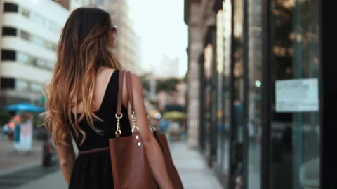 Back view of young beautiful woman with shopping bags walking through the street Stock Footage