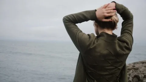 Back view of young blonde woman standing on shore of sea and dreaming Stock Footage