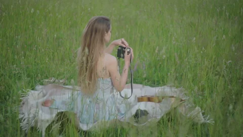 Back view of young brunette lady sitting on green meadow and taking photos on Stock Footage 134895164