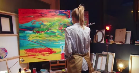 Back view of young Caucasian blonde talented female painter looking at finished Stock Footage 149579604