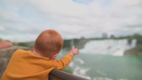 Back view of young child wearing yellow sweater, gazing at breathtaking Niagara Stock Footage 293943159