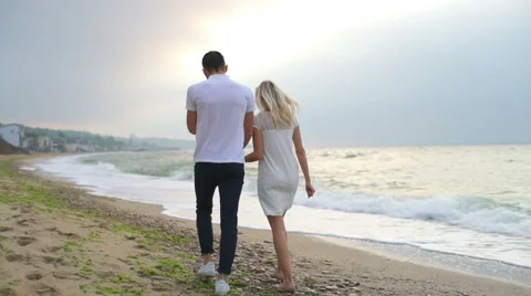 Back view young couple holding hands and walking along the sea slow motion Video stock 65203407