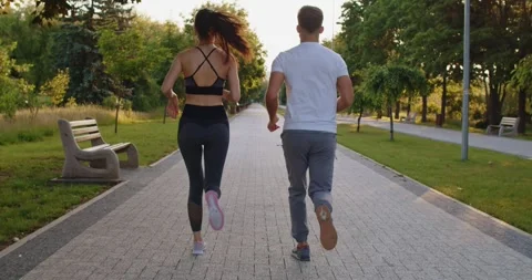 Back view of young couple jogging side by side in park, enjoying outdoor workout Stock Footage 331302338