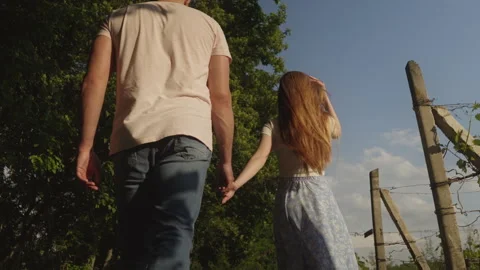 Back view of a young couple in love holding hands while walking along the Stock Footage 250076787