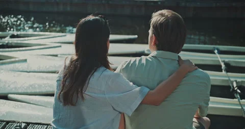 Back view of young couple sitting on the dock enjoying sunshine Video stock 221317857