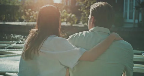Back view of young couple sitting on the dock enjoying sunshine Stock Footage 221317898