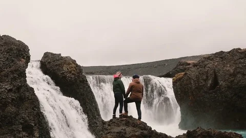 Back view of young couple standing on a rock and looking on a powerful waterfall Stock Footage 82986152
