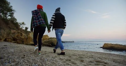 Back view on the young couple strolling on the rocky seacoast near sea. The cold Fotos Stock