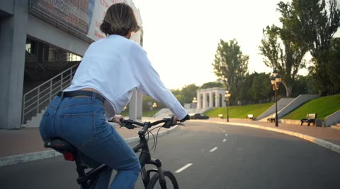 Back view young female riding a bike through the park in sunlight Stock Footage 68346191
