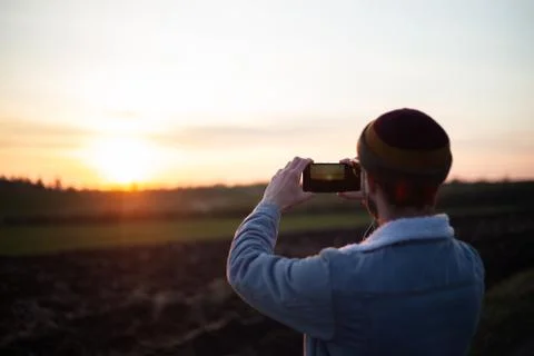 Back view of young guy take pictures of sunset by smartphone. Stock Photos