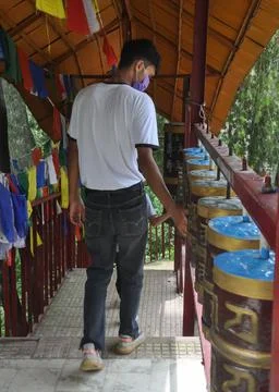 Back view of a young guy wearing face mask with turning Buddhist prayer wheel  Stock-Fotos