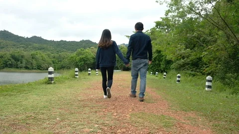 Back view of  Young man and woman walking holding hands enjoying Stock Footage 114438591
