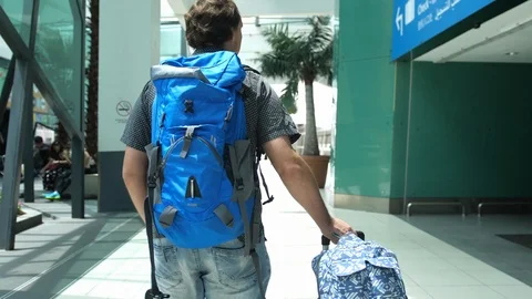 Back of view of young man with backpack pulling suitcase in modern airport Video stock 98616830