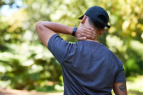 Back view of young man rubbing neck, outdoor exercise, pain and injury Stock Photos