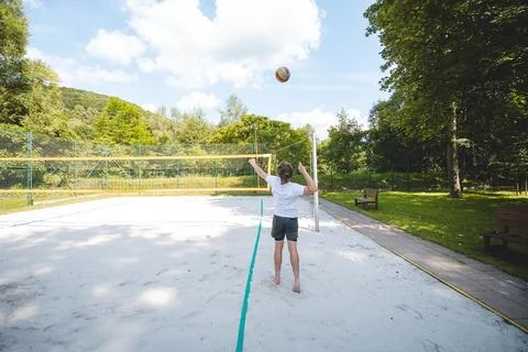 Back view of a young man serving a volleyball on a sand court under a bright  Stock Photos