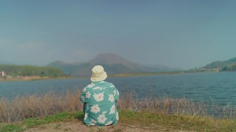Back view of young man sitting by the lakeshore, tossing a stone into the water. Stock Footage 301509559