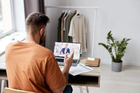 Back view of young man sitting in front of laptop with tutor on screen Foto stock