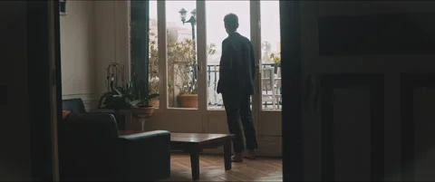 Back view of a young man standing by the window looking outside Video stock 203585995