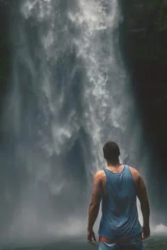Back view of young man standing in front of powerful Nungnung waterfall on Ba Stock Photos