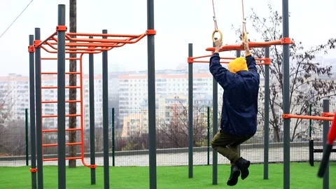 Back view of young man training outside on gymnastic gym rings enjoying healthy  스톡 동영상 166087500