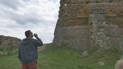 Back view of young man vaping and looking at ancient ruins outdoors Видео 156667741