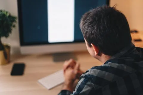 Back view of a young man working from home office, looking at the computer sc Stock Photos