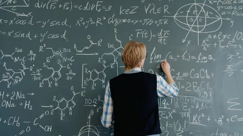 Back view of young maths teacher writing equations on chalkboard in classroom Stock Footage 125078796