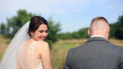 Back view of young newlyweds walking on sunny background smiling looking at Video stock 143175124