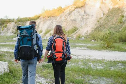 Back view of young pair backpackers with big backpacks holding hands and wa.. Stock Photos
