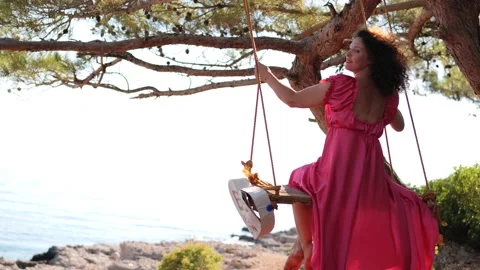 Back View at Young Resting woman in beautiful pink long dress swinging on a Stock Footage 208317543