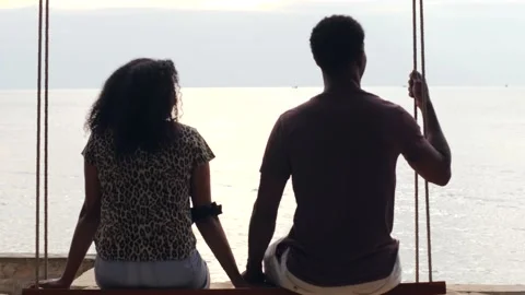 Back view of young sweet couple sitting on a swing relaxing in front of the sea. Stock Footage 148133884