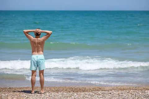 Back view of a young white man looks out over the turquoise sea. Stock Photos